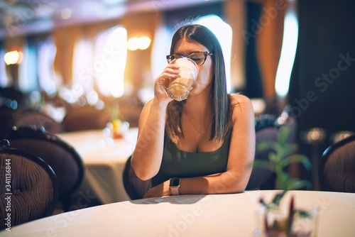 Young beautiful woman drinking glass of coffee sitting at restaurant