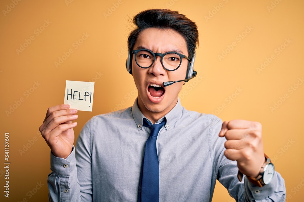 Young handsome chinese call center agent man overworked using headset asking for help annoyed and frustrated shouting with anger, crazy and yelling with raised hand, anger concept Young handsome chinese call center agent man overworked using headset asking for help annoyed and frustrated shouting with anger, crazy and yelling with raised hand, anger concept