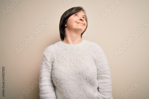 Young down syndrome woman standing over isolated background looking away to side with smile on face, natural expression. Laughing confident.