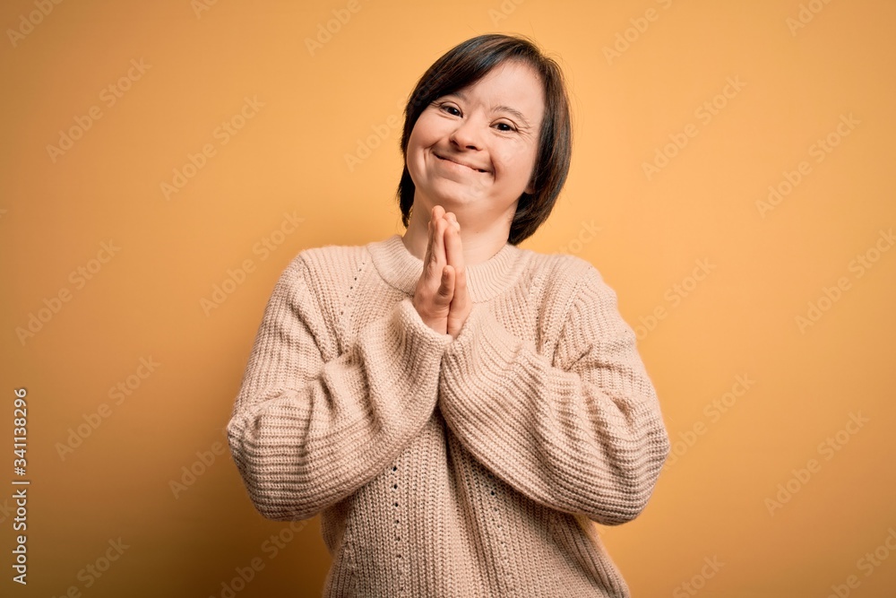 Young down syndrome woman wearing casual sweater over yellow background praying with hands together asking for forgiveness smiling confident. Young down syndrome woman wearing casual sweater over yellow background praying with hands together asking for forgiveness smiling confident.