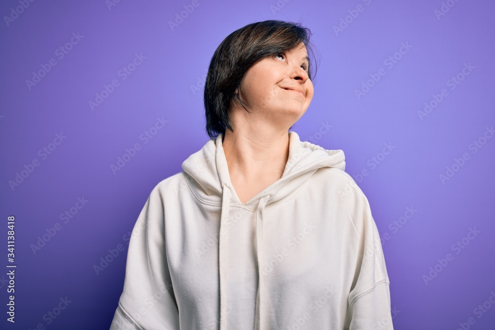 Young down syndrome sports woman wearing fitness sweatshirt over purple background looking away to side with smile on face, natural expression. Laughing confident. Young down syndrome sports woman wearing fitness sweatshirt over purple background looking away to side with smile on face, natural expression. Laughing confident.