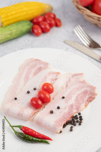 Pork belly sliced ​​on a white plate with pepper seeds and tomatoes.