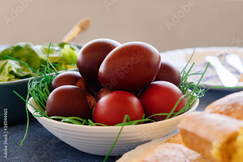 Close up view on red colored easter eggs in bowl with cornbread corn pone in a white plate on the table and the blue bowl with fresh green salad organic in background