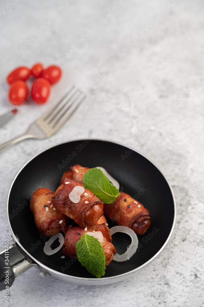 Sausage wrapped in pork belly in a frying pan. Sausage wrapped in pork belly in a frying pan.