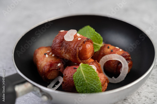 Sausage wrapped in pork belly in a frying pan.