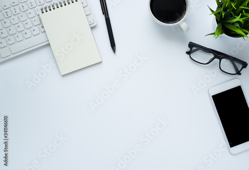 Workplace in office with white desk. Top view from above of keyboard with notebook and coffee. Space for modern creative work of designer. Flat lay with blank copy space. Business and finance concept.