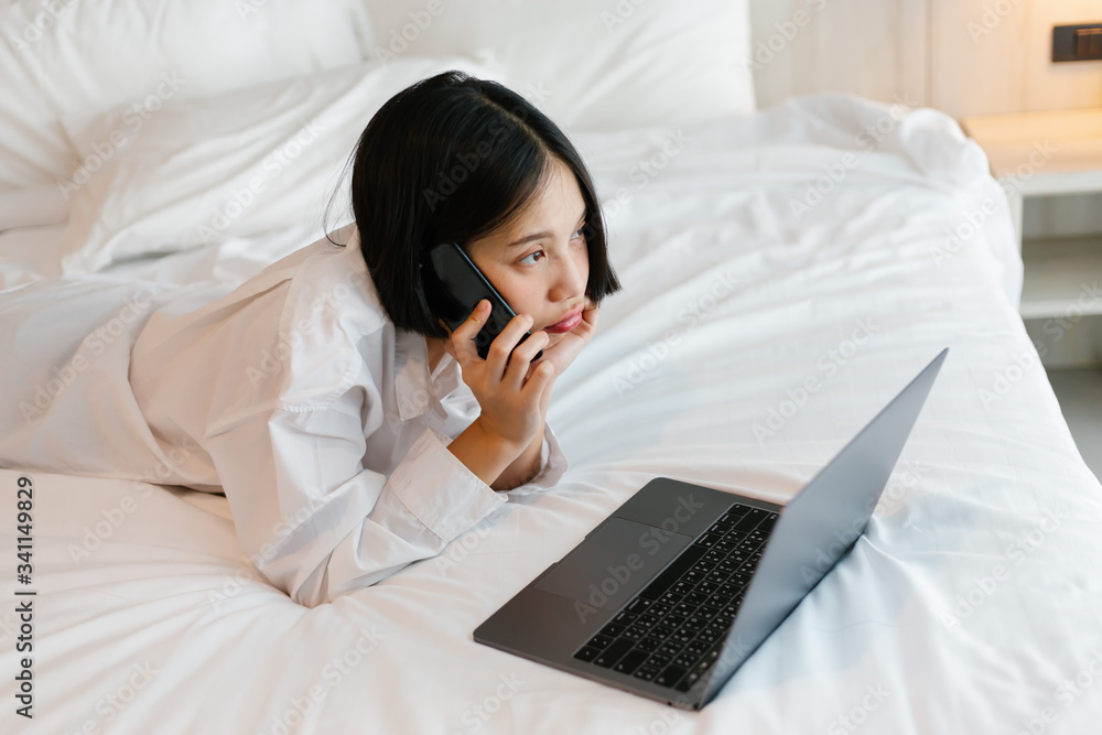 Beautiful asian female in white shirt using mobile phone while working on bed. work from home concept. Beautiful asian female in white shirt using mobile phone while working on bed. work from home concept.