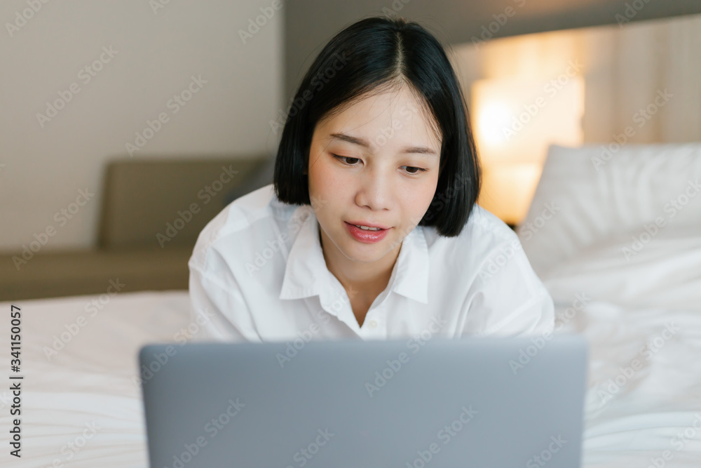 Beautiful asian female in white shirt using laptop while working on bed. work from home concept. Beautiful asian female in white shirt using laptop while working on bed. work from home concept.