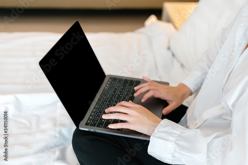 Focusing hand female in white shirt using laptop while working on bed. work from home concept.