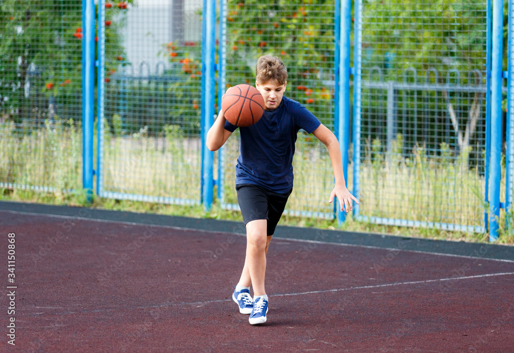 Cute boy in blue t shirt plays basketball on city playground. Active teen enjoying outdoor game with orange ball. Hobby, active lifestyle, sport for kids. Cute boy in blue t shirt plays basketball on city playground. Active teen enjoying outdoor game with orange ball. Hobby, active lifestyle, sport for kids.