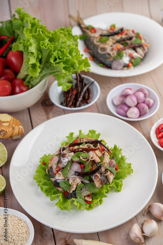 Deep-fried mackerel topped with galangal, pepper, mint, red onion in a white dish.