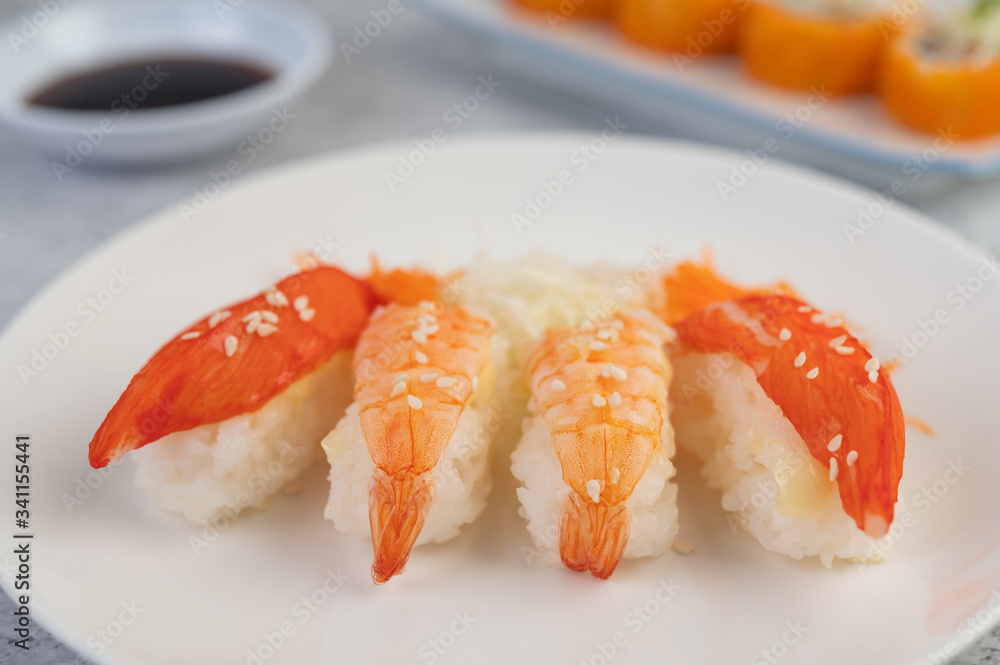 Sushi is on a plate with dipping sauce on a white cement floor. Sushi is on a plate with dipping sauce on a white cement floor.