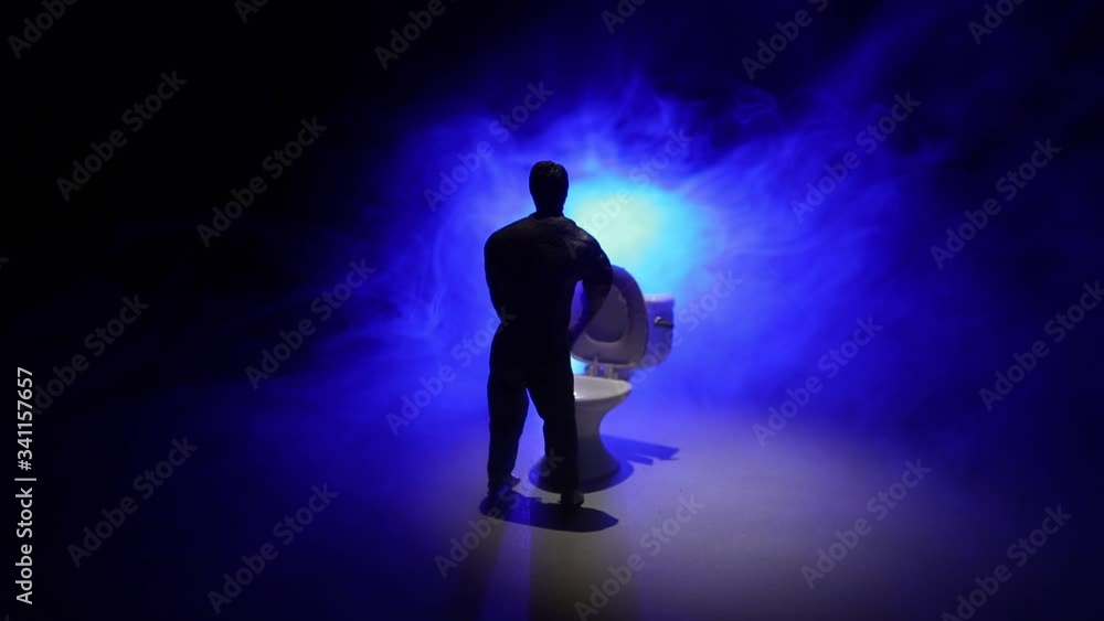 Creative concept. Miniature white toilet bowl on dark foggy background. Man peeing. Selective focus Creative concept. Miniature white toilet bowl on dark foggy background. Man peeing. Selective focus