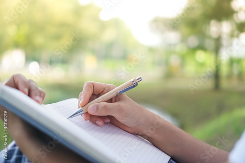 Woman hand writing down in small white memo notebook for take a note not to forget or to do list plan.