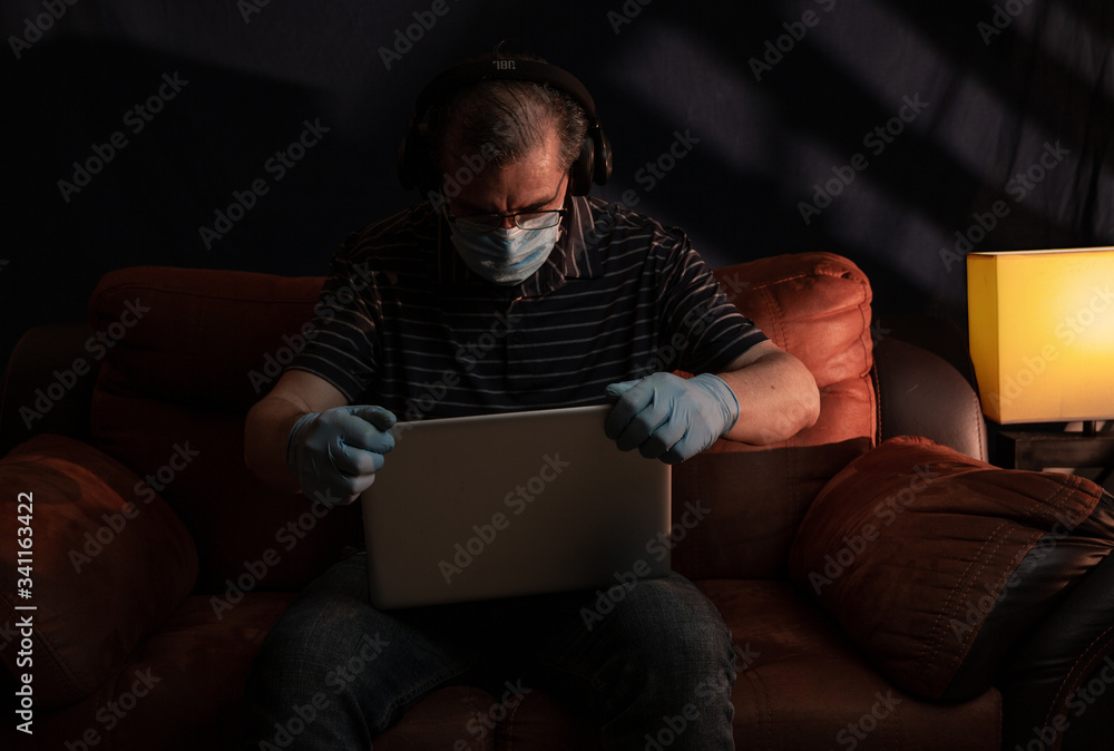 Middle aged man working at home on his computer for the coronavirus using protective equipment such as gloves and mask Middle aged man working at home on his computer for the coronavirus using protective equipment such as gloves and mask