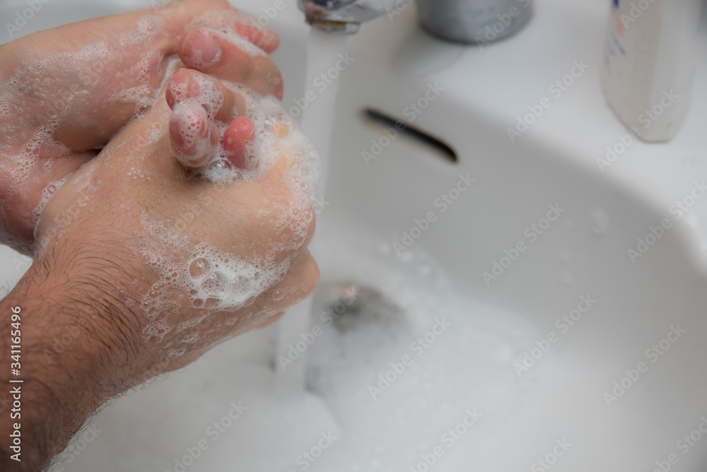 Manos de hombre frontandose con jabon para lavarse y prevenir el coronavirus. grifo metalico y lavabo blanco de fondo. Manos de hombre frontandose con jabon para lavarse y prevenir el coronavirus. grifo metalico y lavabo blanco de fondo.