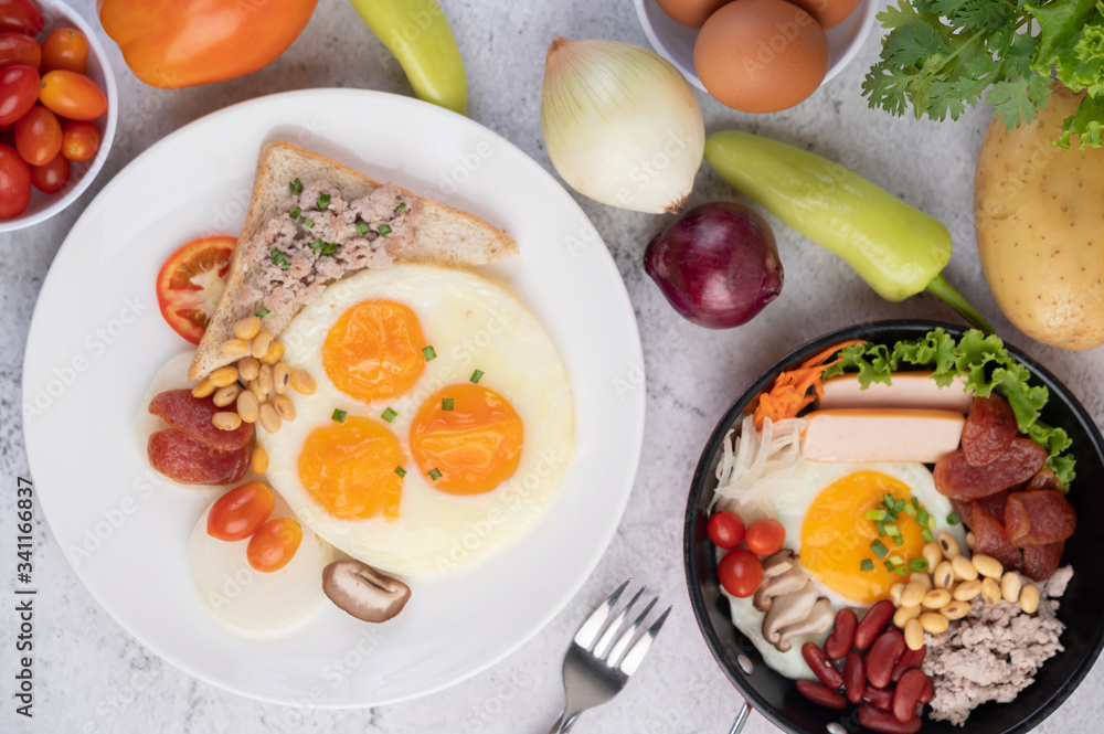 Breakfast consists of fried eggs, sausage, minced pork, bread, red beans and soy on a white plate. Breakfast consists of fried eggs, sausage, minced pork, bread, red beans and soy on a white plate.