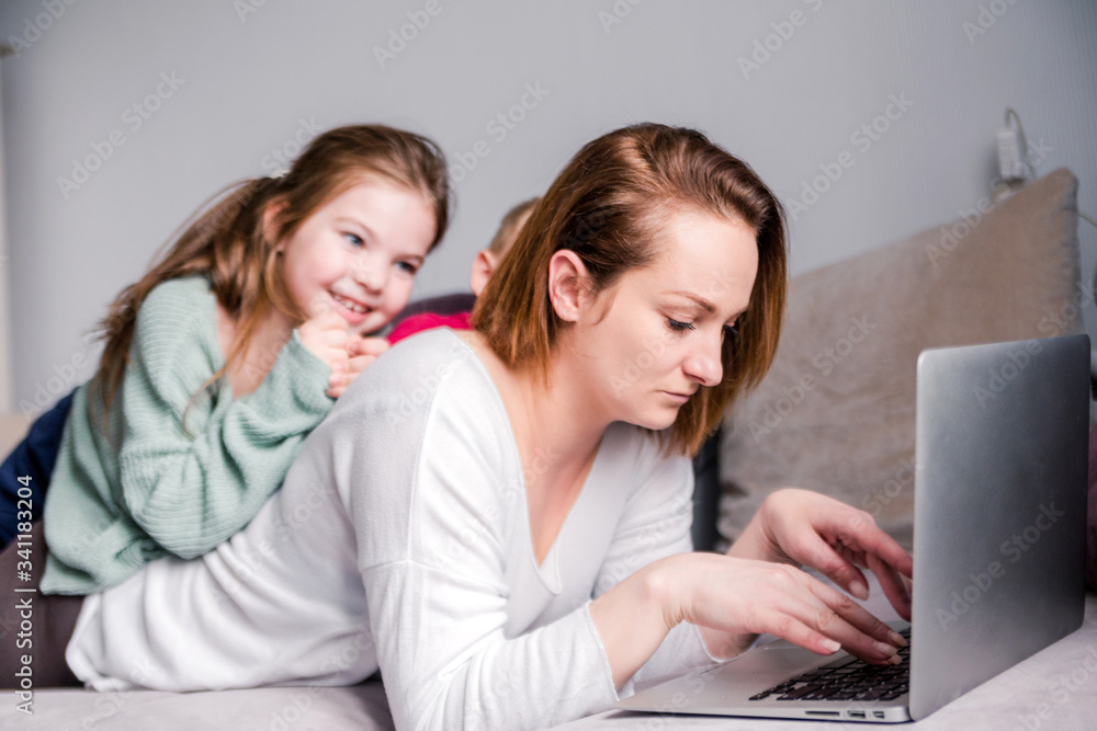 Young women works at home with laptop along with two children.Children want to communicate with mother, make noise and interfere with work.Self-isolation during coronovirus pandemic Young women works at home with laptop along with two children.Children want to communicate with mother, make noise and interfere with work.Self-isolation during coronovirus pandemic