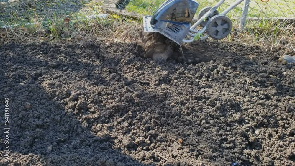 Home gardening - Preparing garden soil using electric soil cultivator or tiller to soften and break apart clumps of soil at back yard garden. Home gardening - Preparing garden soil using electric soil cultivator or tiller to soften and break apart clumps of soil at back yard garden.