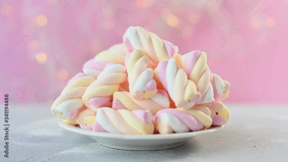 colourful marshmallows heap lies on small white plate against blurry flashing lights on pink background close view colourful marshmallows heap lies on small white plate against blurry flashing lights on pink background close view