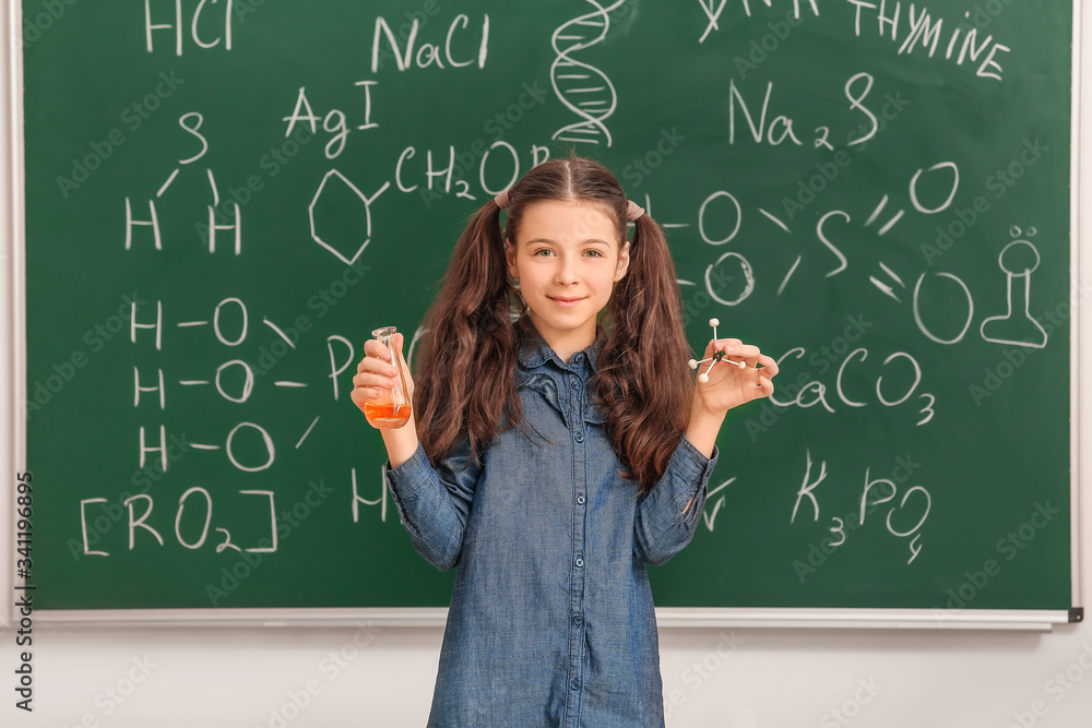 Cute little girl near blackboard at chemistry lesson in classroom