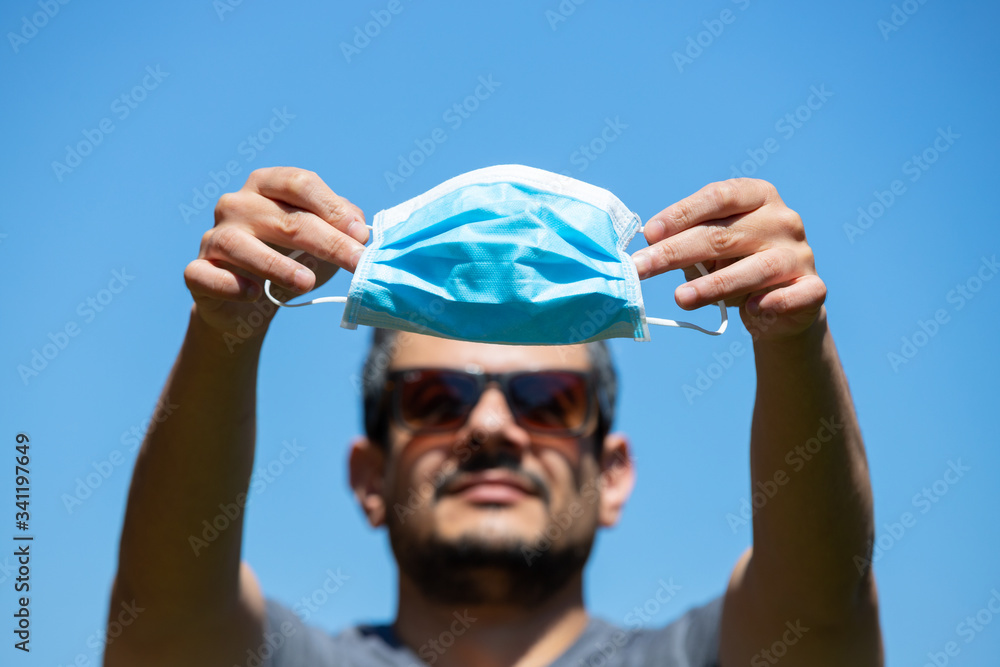 Man standing outdoors holds up a flu mask, selective focus on mask. Face masks are necessary against spread of Covid19. Man standing outdoors holds up a flu mask, selective focus on mask. Face masks are necessary against spread of Covid19.