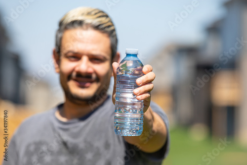 Happy man holding a water bottle, while standing outdoors. Selective focus on water bottle.