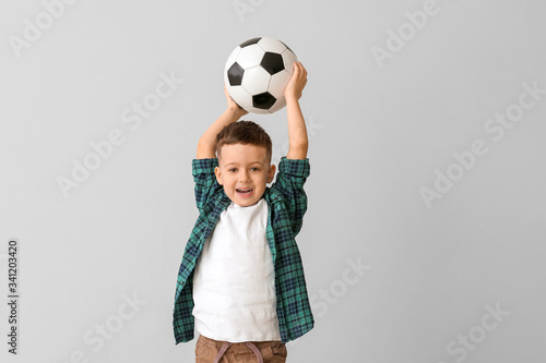 Cute little boy with soccer ball on grey background