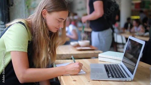 side portrait female writes in notebook. concentrated young beautiful white fwoman writes notes study distance or work as freelancer. pretty girl works remotely in coffee shop, hard working goals photo