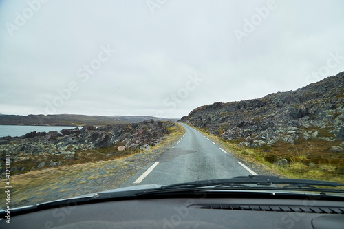 View from car window on the road and pity strange landscape with a mountains, rocks and cloudy sky. Landscape through windscreen in Norway
