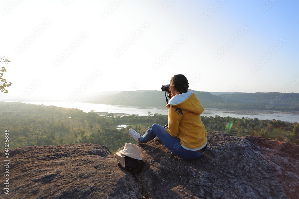 Woman sitting and taking pictures at the cliff in Pha Tam National Park, Ubon Ratchathani, Thailand.