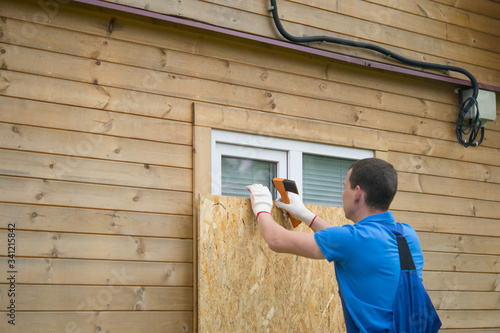 Fotografie worker, boarded up the window of the house with a protective shield made of wood