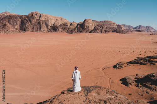 A man with local Arab dress standing on rock and looking to Wadi Rum desert in Jordan, Arab