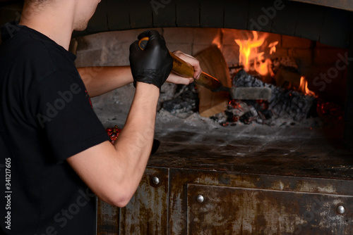 Young man cooking food in a professional stone oven with red fire inside the oven. Professional cook in a restaurant.