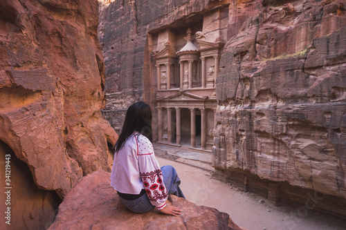 A woman traveler sitting at viewpoint of Petra ancient city looking at the Treasury or Al-khazneh, Jordan, Arab