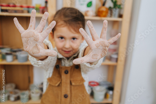 Little girl in a pottery workshop with clay-stained hands photo