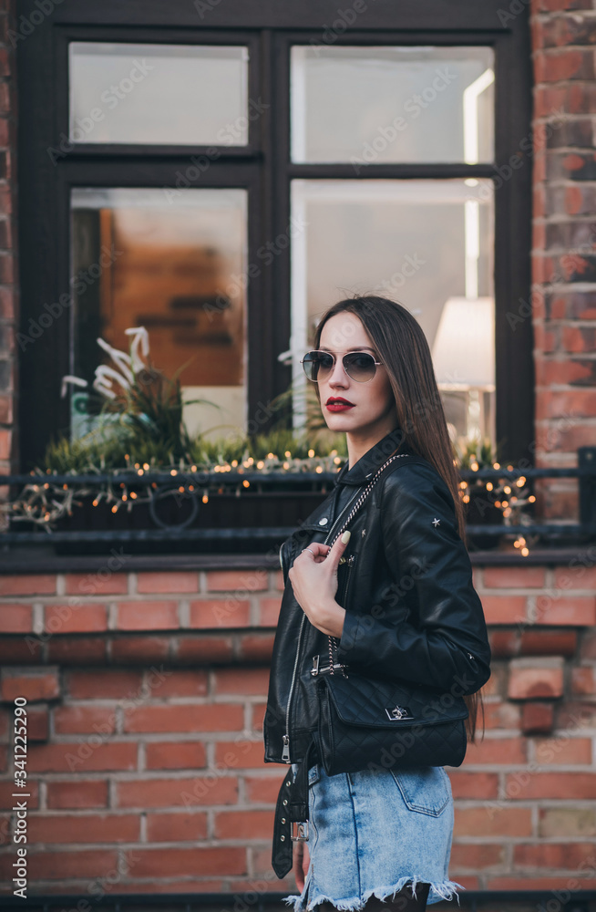 Young beautiful girl in stylish wear and sunglasses walking in street