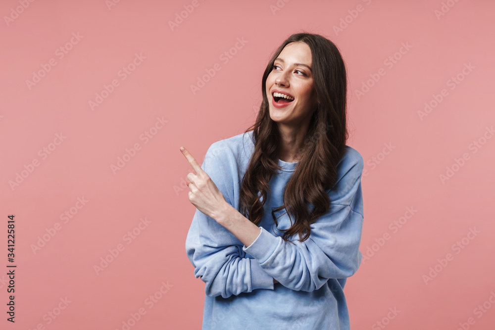 Image of young woman smiling and pointing finger at empty space Image of young woman smiling and pointing finger at empty space