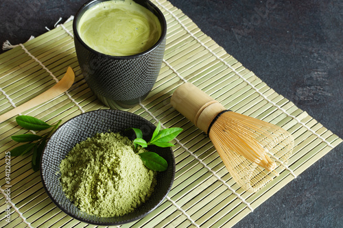 Organic green matcha tea and tea accessories on japanese mat on black background. Japanese tea ceremony concept.
