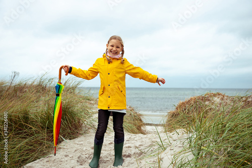 Cheerful little girl staying on beach with colorful ambrella on Baltic sea at windy weathe photo