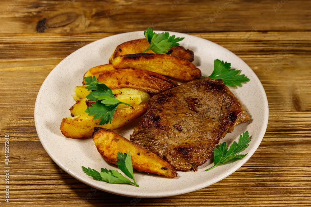 Fried beef steak with potato wedges on wooden table Fried beef steak with potato wedges on wooden table