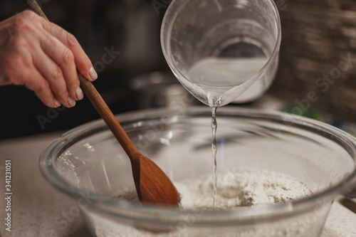 Pouring water into dry dough mixture while mixing with wooden spoon