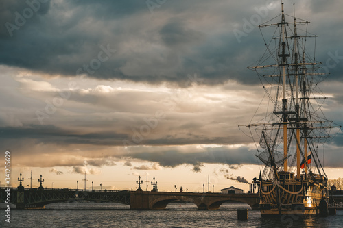 The ship at the embankment in the sunset rays, the dark sea and sky, Vintage frigate on the banks of the Neva. Ship off the coast of St. Petersburg. Flag of Russia is fixed on a vintage frigate. 