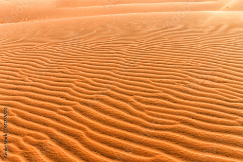Orange sand lies beautifully in waves at sunset. Sand texture close-up. Hills of yellow sand in Vietnam.