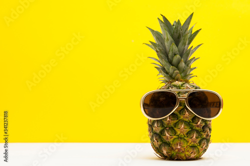 Summertime pineapple fruit with sunglasses against a bright yellow background