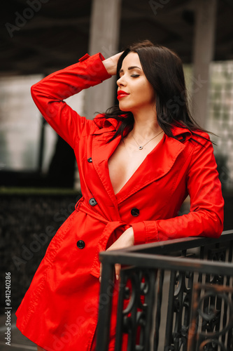 
Beautiful young, sexy woman with red lips in a red cloak, dressed on her naked body, open neckline, chest after plastic surgery, beautiful breasts 3 sizes, against the black walls, in the city