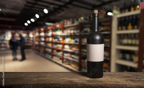 Bartender or male cavist standing near the shelves of wine bottles holds a glass of wine, looks at tint and smells flavor of wine in glass. photo