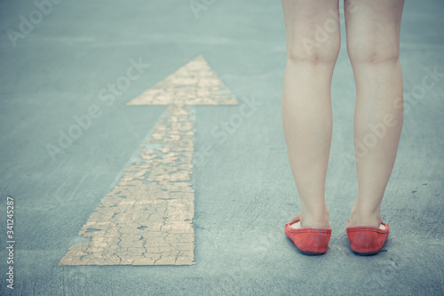 Vintage tone of Girl wear red shoes walking towards with yellow traffic arrow signage on an asphalt road