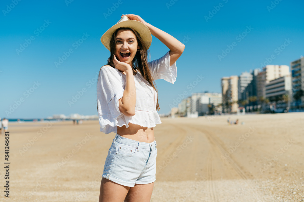 stormy joy on the face of a girl in a cowboy hat. opening her mouth from a storm of emotions, she holds a hat with her hand. behind the building, beach sand