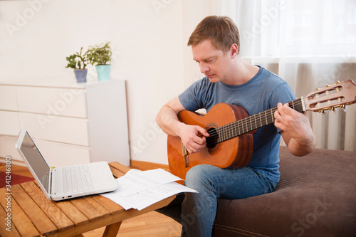 Man playing acoustic guitar and watching online lesson on laptop while practicing at home. Stay home. quarantine. Online training, online classes. 